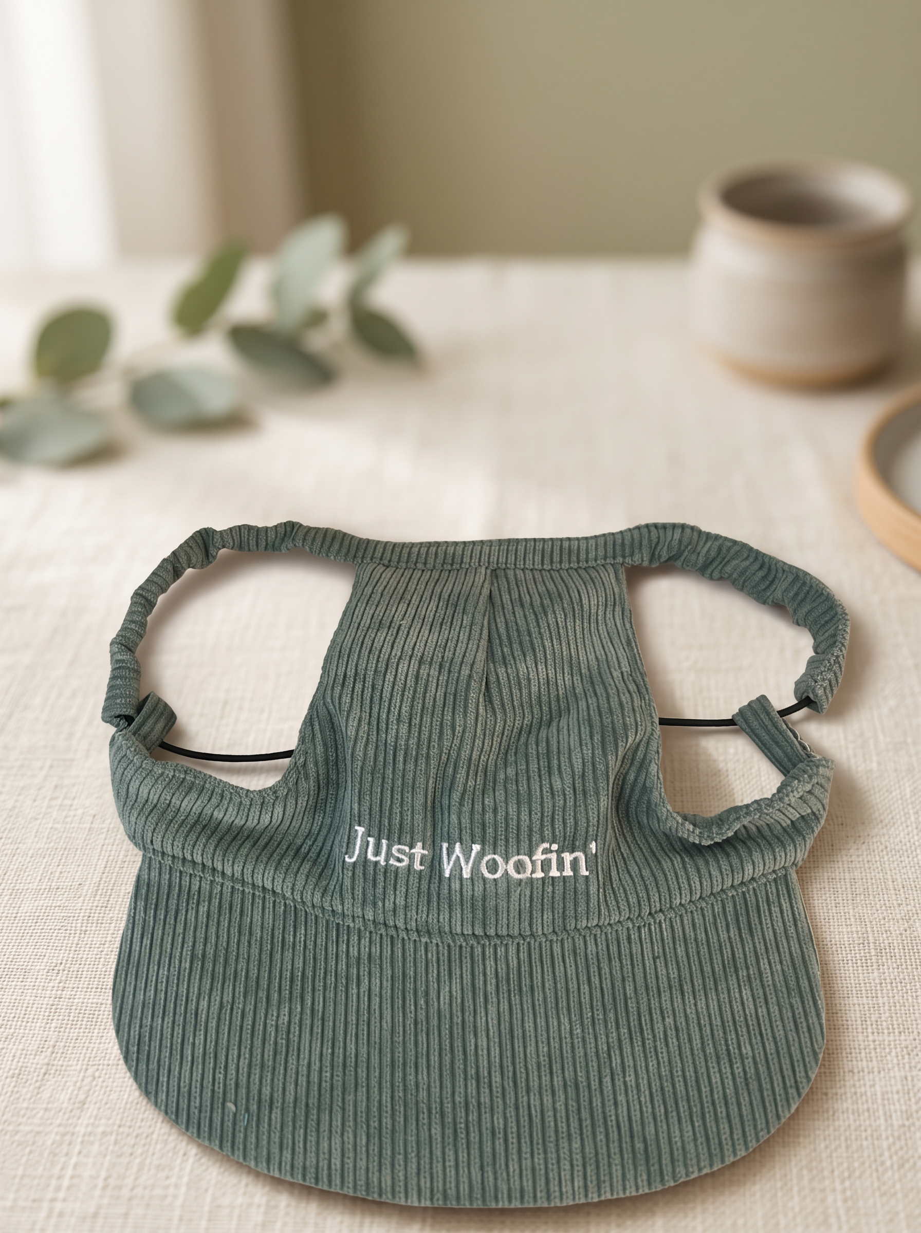 Just Woofin' sage green corduroy dog hat on cream linen with eucalyptus